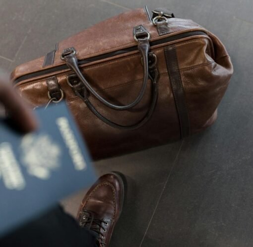 Brown leather bag with passport in an airport setting, ideal for travel and fashion themes.