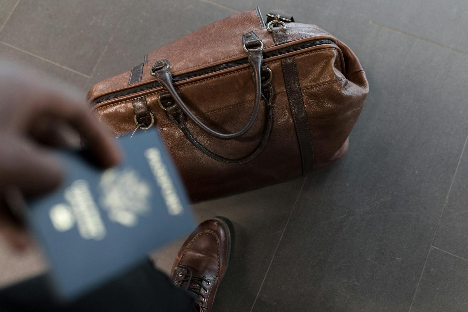 Brown leather bag with passport in an airport setting, ideal for travel and fashion themes.