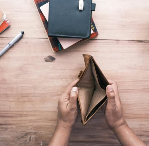 Top view of hands holding an open empty wallet on a wooden desk with notebooks and pen.