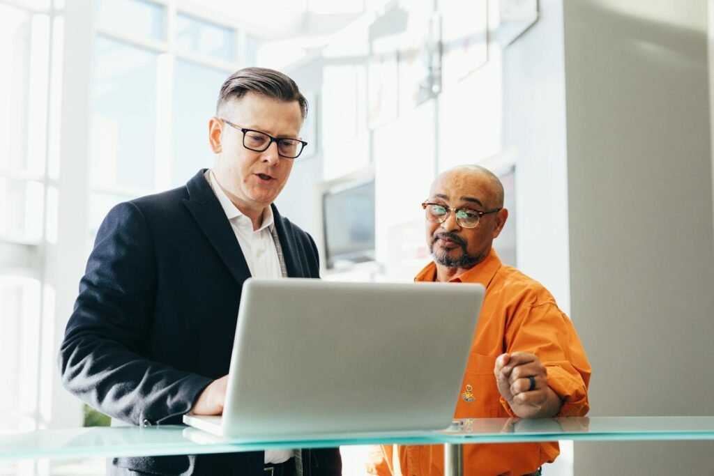 Two business professionals engaged in a collaborative discussion over a laptop in a modern office setting.