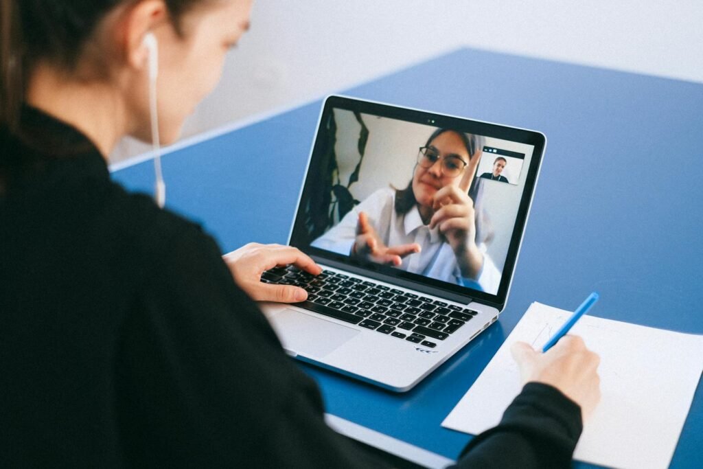 Woman participating in a virtual meeting, taking notes during a video conference on a laptop.