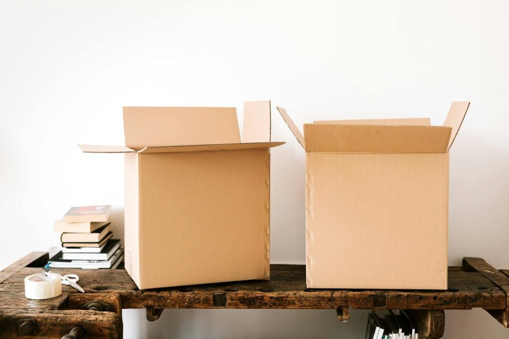 Opened carton boxes and stacked books placed on shabby wooden desk with tape against white wall