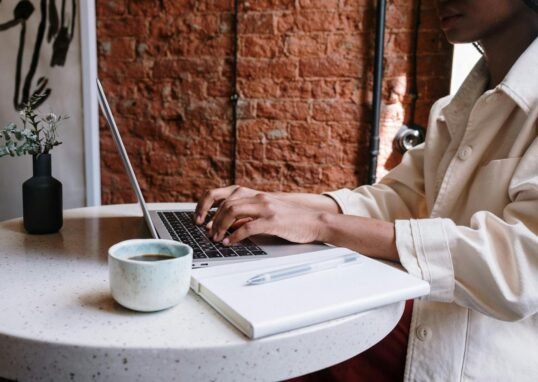 Woman working on a laptop with coffee in a cozy café, highlighting a productive and modern vibe.