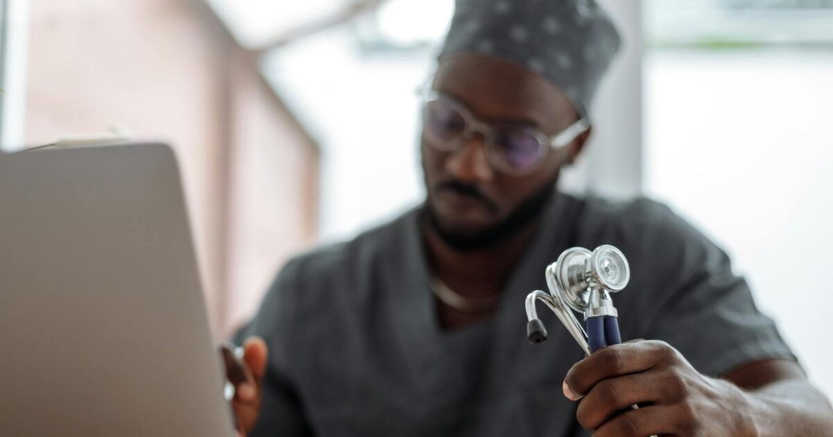 Focused African American doctor in scrubs working with laptop and stethoscope.