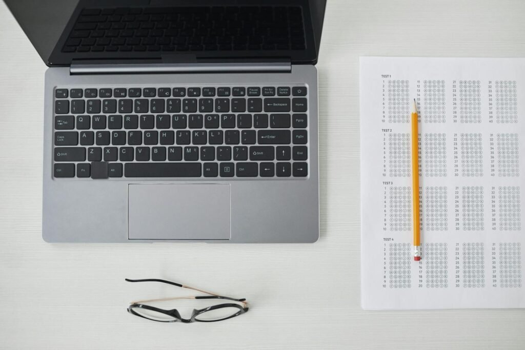 Flat lay of a laptop, exam sheet, and pencil on a white desk, perfect for education and technology themes.