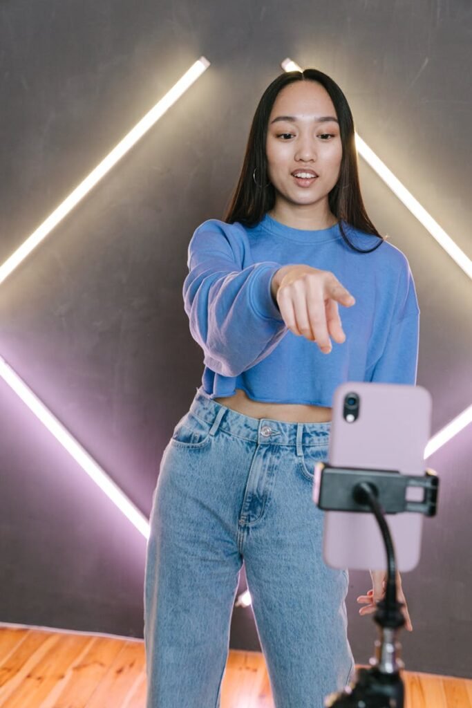 Asian woman streaming content using smartphone and tripod in modern setup.