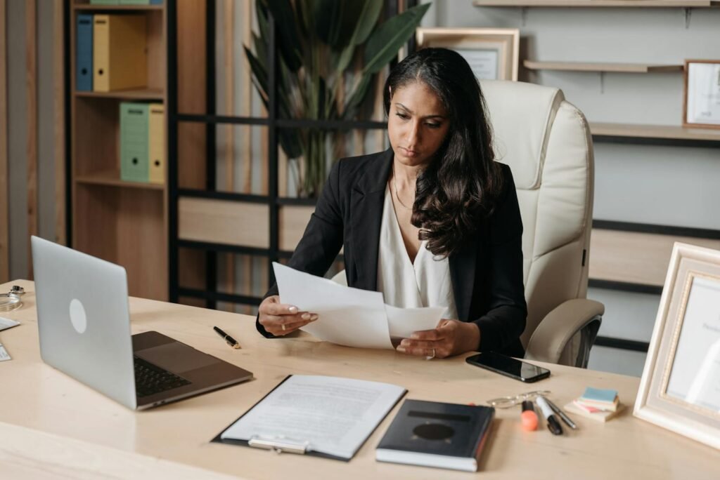 Business woman focused on paperwork at office desk, reviewing documents.