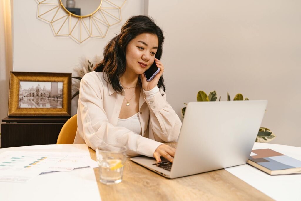 Young woman multitasking with laptop and cellphone in home office setup.