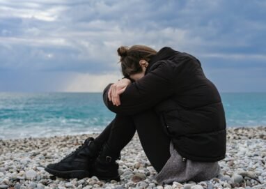 a woman sitting on a rocky beach with her head in her hands