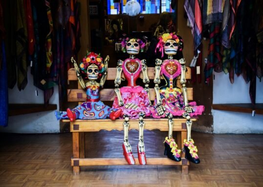 three Frida Kahlo skeleton dolls sitting on bench