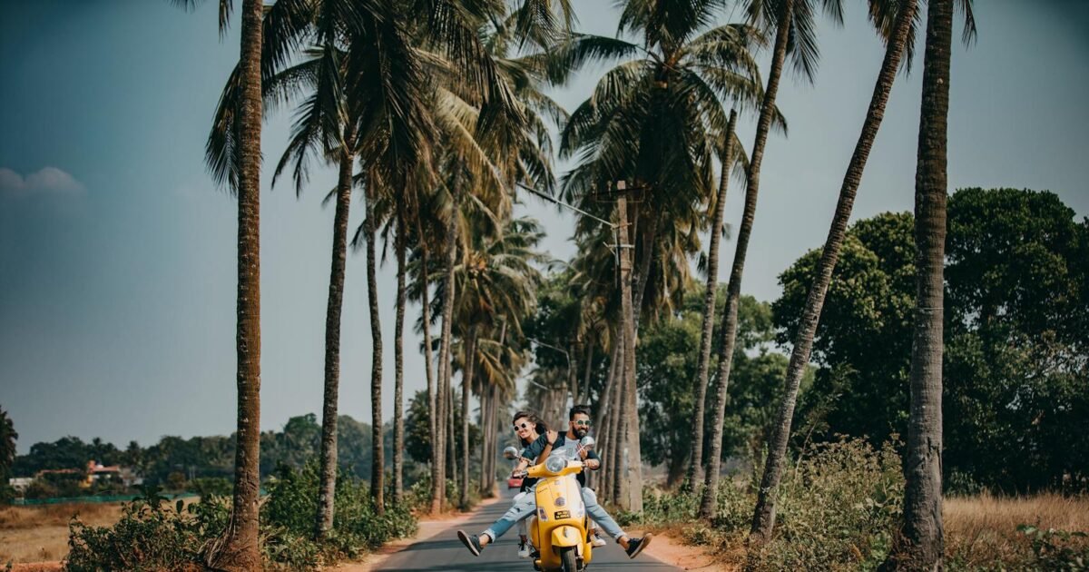 A joyful couple rides a yellow scooter through a scenic palm-lined road, capturing the essence of tropical travel and adventure.