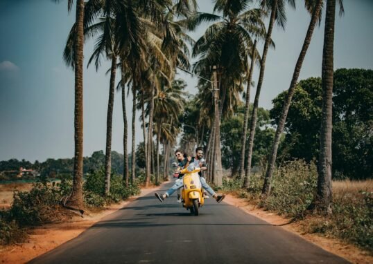 A joyful couple rides a yellow scooter through a scenic palm-lined road, capturing the essence of tropical travel and adventure.